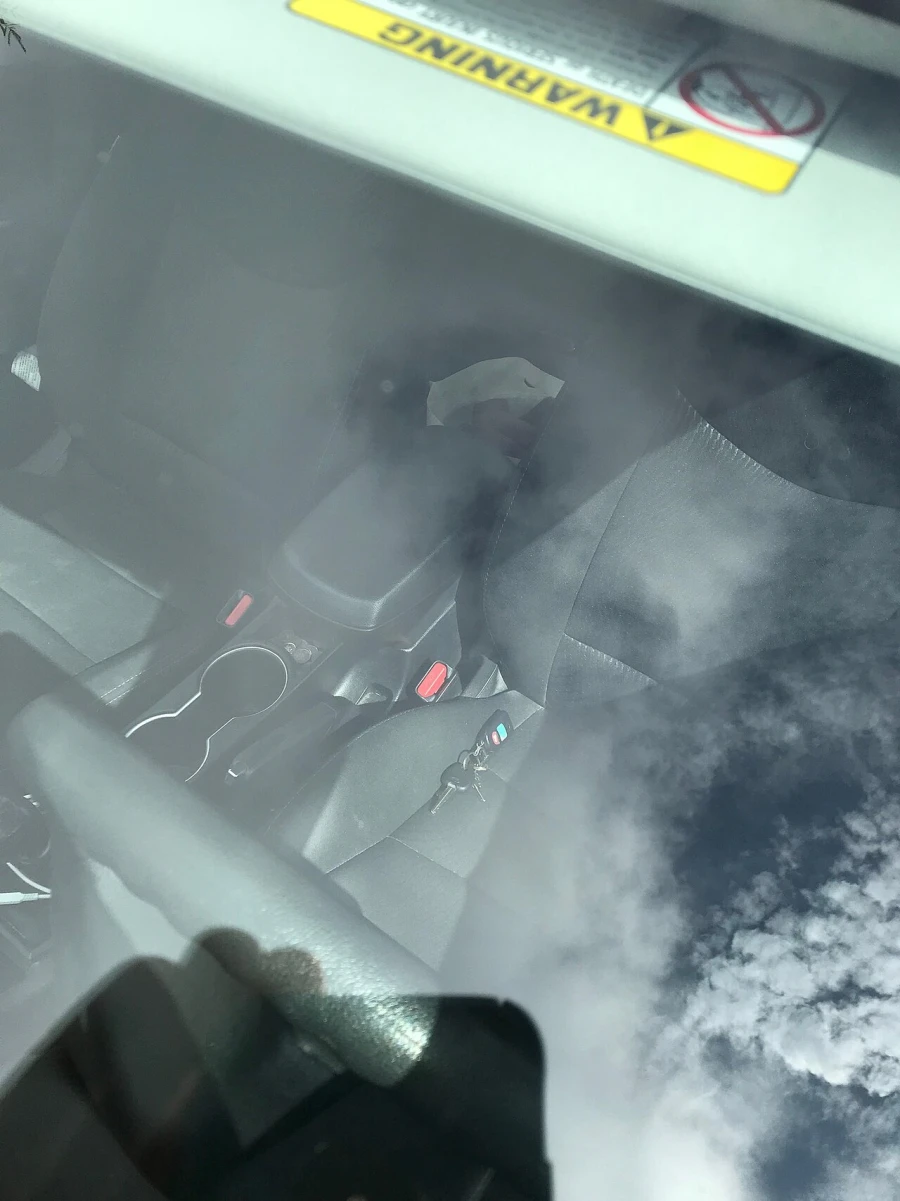 A ring of car keys with a remote fob lying on the seat of a locked car, seen through the window glass