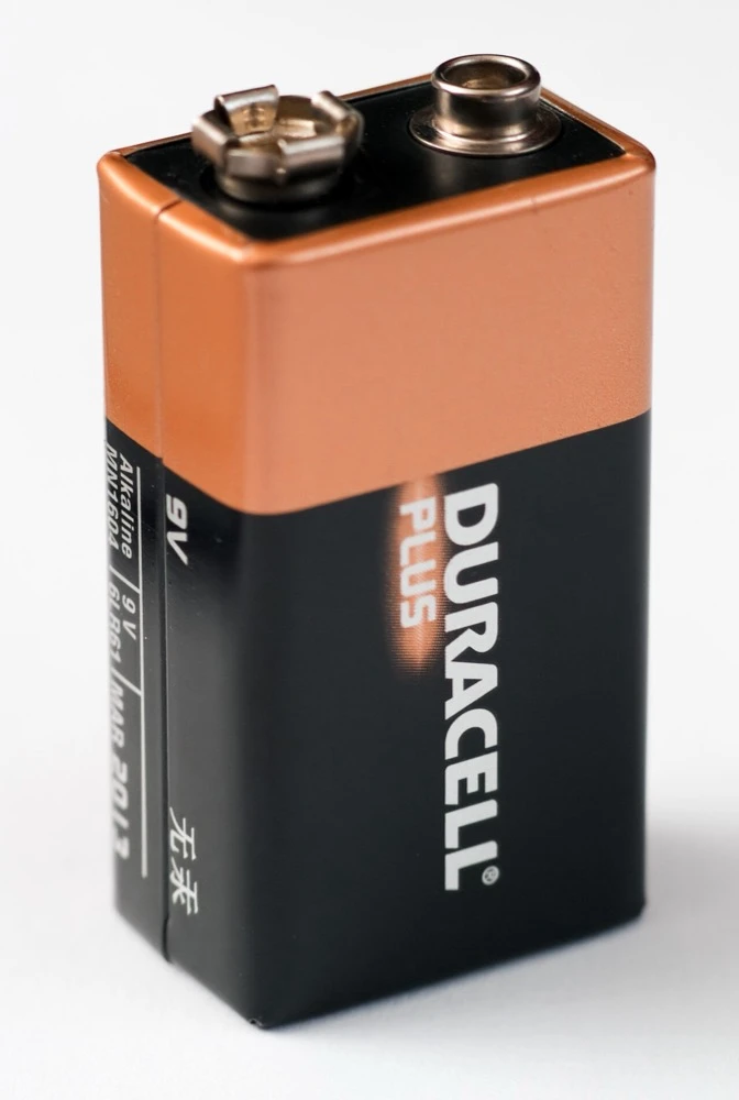 A Duracell 9 volt alkaline battery standing upright, with its two snap terminals on top