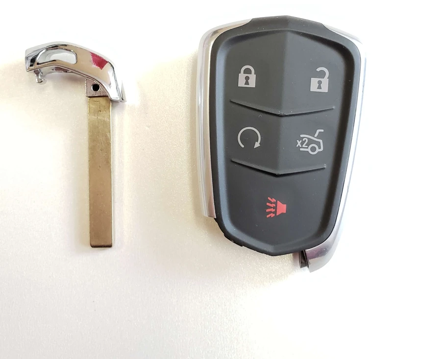 A Cadillac smart key fob with lock, unlock, remote start, trunk and panic buttons, next to its metal emergency key blade