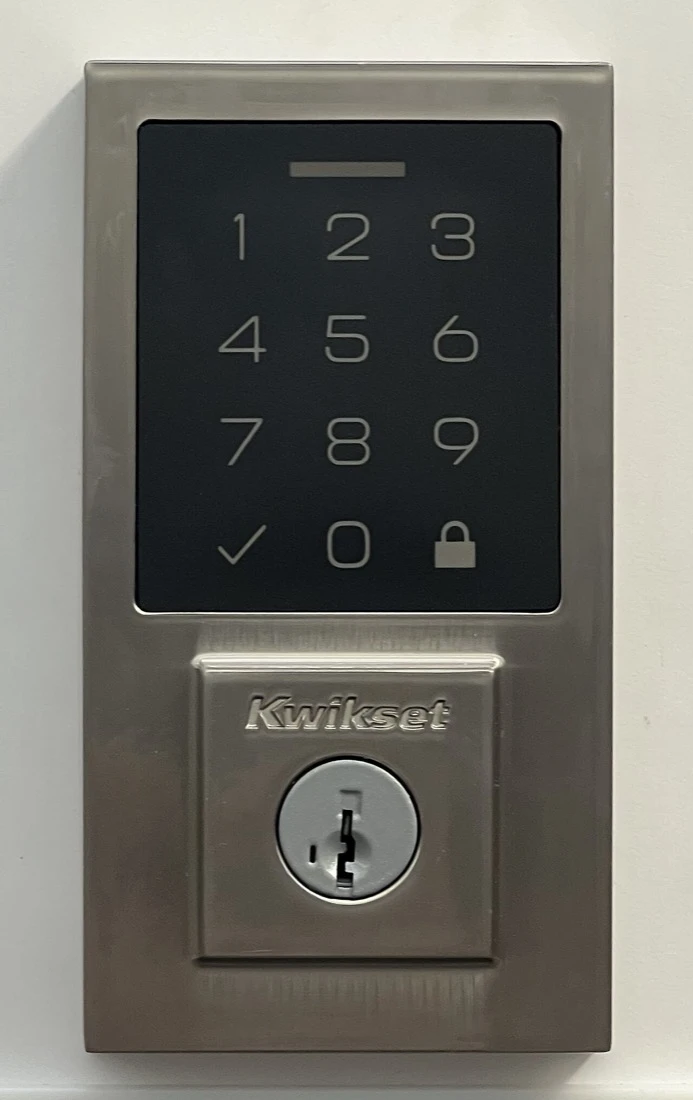A Kwikset touchscreen keypad deadbolt on a white door, with a key cylinder below the number pad